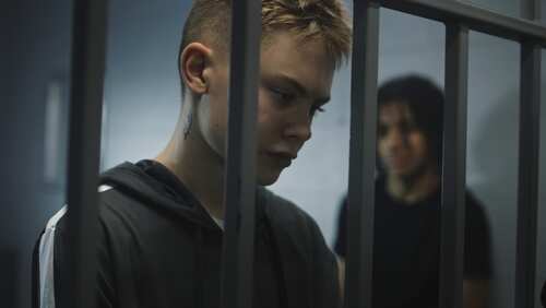 Warden,Takes,Off,Handcuffs,From,Young,Prisoner.,Multi,Ethnic,Teenagers Two young individuals in a detention setting, one looking down and the other in the background