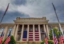 Supreme Showdown: Women’s Sports On The Line Historic building with large American flag and multiple flags in front