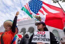 Two women at a protest holding flags and a sign against deportation