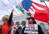 Two women at a protest holding flags and a sign against deportation