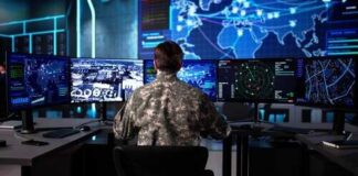 Military personnel monitoring multiple screens in a command center