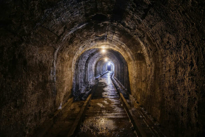 2256308279 A dimly lit underground tunnel with wet stone walls and railway tracks
