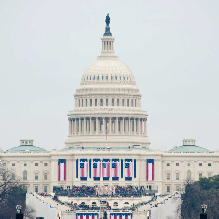 The U.S. Capitol building adorned with flags during a national event with a large crowd in front
