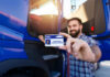 Man holding a commercial driver's license in front of a blue truck