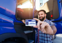 Man holding a commercial driver's license in front of a blue truck