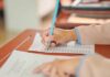 A student's hand holding a pencil while writing on a sheet of paper