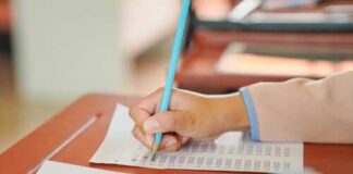 A student's hand holding a pencil while writing on a sheet of paper
