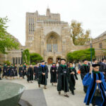 Graduates and faculty in academic regalia walking on a university campus