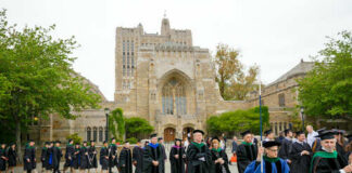 Graduates and faculty in academic regalia walking on a university campus