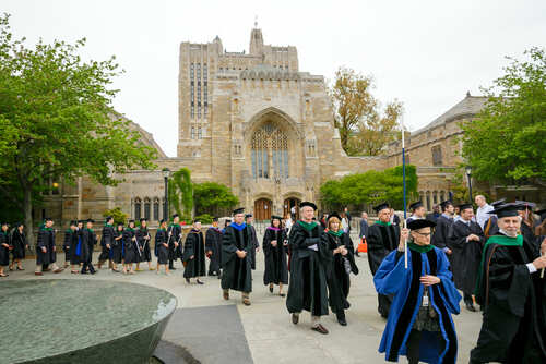 Graduates and faculty in academic regalia walking on a university campus