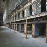 Triple Execution Shock — Same Day Interior view of an abandoned prison with empty cells and peeling paint