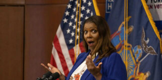Person speaking with surprised expression at podium flags behind
