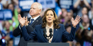 Woman speaking at podium, man standing behind.