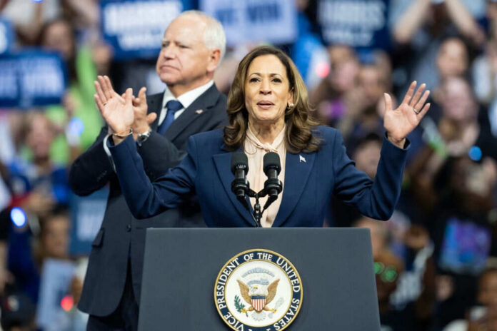 Woman speaking at podium, man standing behind.