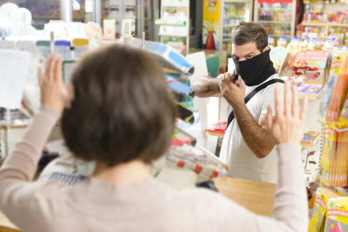 A masked individual threatening a store clerk during a robbery