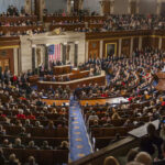 Socialist Surge Corners Jeffries, Schumer People in a large government assembly hall meeting
