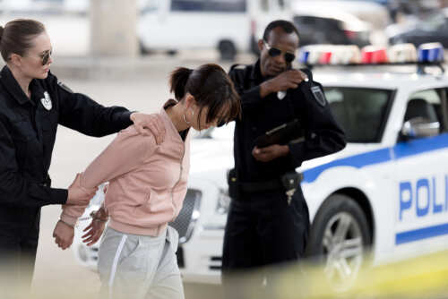 Policewoman,Holding,Arrested,Young,Woman,While,Her,Partner,Talking,On Police officers arresting a suspect in an urban environment