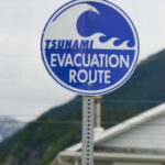 Pre-Dawn 7.7 Quake: Now Tsunami Panic Sign indicating tsunami evacuation route with a wave graphic