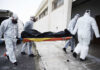 Emergency responders in hazmat suits carrying a body on a stretcher