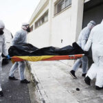 Emergency responders in hazmat suits carrying a body on a stretcher
