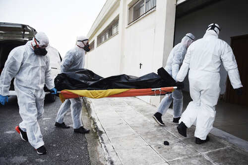 Emergency responders in hazmat suits carrying a body on a stretcher