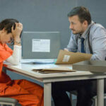 A detective interrogating a prisoner in an orange jumpsuit at a table