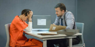 A detective interrogating a prisoner in an orange jumpsuit at a table