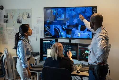Agents,Of,Fbi,Discussing,Record,Of,Security,Camera,With,Fraud Three professionals analyzing security footage on multiple screens