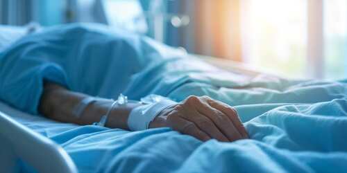 Closeup,Of,Patient's,Arm,With,Iv,Drip,In,A,Hospital A patient's hand resting on a hospital bed with an IV line attached