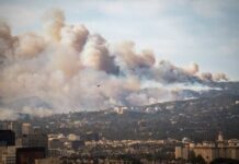 Human Spark, City Inferno A wildfire producing thick smoke over a city landscape with a helicopter in the sky