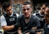 A man with tattoos being arrested by ICE agents in an urban environment