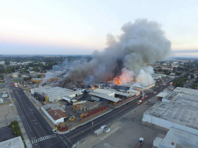 1062550499 A large industrial fire with thick smoke rising into the sky and firefighters responding