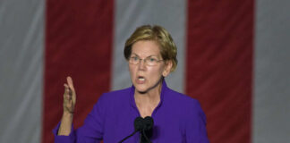 Person speaking at podium with hand raised.