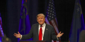 Man speaking at a podium with American flags.