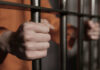 Person in orange holding jail bars tightly