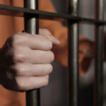 Person in orange holding jail bars tightly