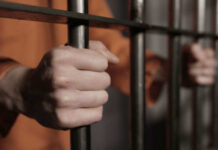 Person in orange holding jail bars tightly