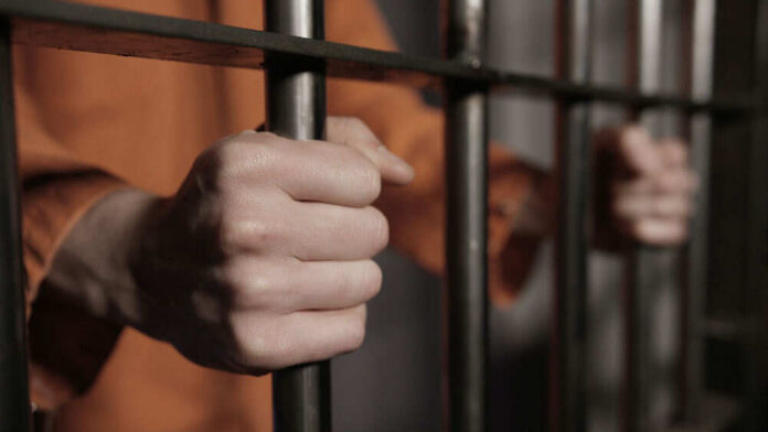 Person in orange holding jail bars tightly
