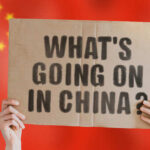 Hands holding a cardboard sign with the text 'What's going on in China?' against a red background with stars