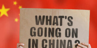 Hands holding a cardboard sign with the text 'What's going on in China?' against a red background with stars