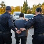 Powerball Millionaire Found Dozing – Then Cuffed Two police officers escorting a handcuffed suspect