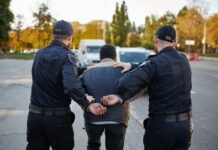 Powerball Millionaire Found Dozing – Then Cuffed Two police officers escorting a handcuffed suspect