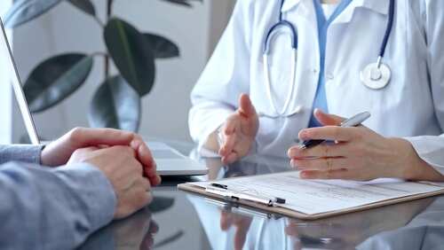 Doctor,Woman,Wearing,White,Medical,Coat,Is,Consulting,Patient,In A doctor discussing with a patient over a clipboard in a medical office