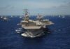 An aircraft carrier surrounded by a fleet of naval ships in the ocean