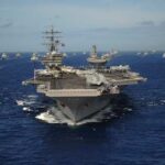 An aircraft carrier surrounded by a fleet of naval ships in the ocean