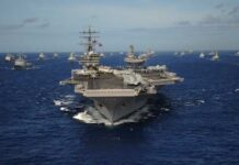 An aircraft carrier surrounded by a fleet of naval ships in the ocean