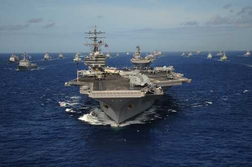 An aircraft carrier surrounded by a fleet of naval ships in the ocean
