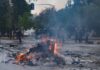 A burning pile of debris in the street during a protest with police in the background