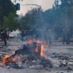A burning pile of debris in the street during a protest with police in the background