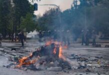 A burning pile of debris in the street during a protest with police in the background
